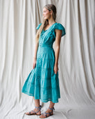Woman wearing a teal dress standing against a white curtain