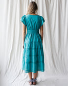 Woman wearing a teal dress standing against a white curtain