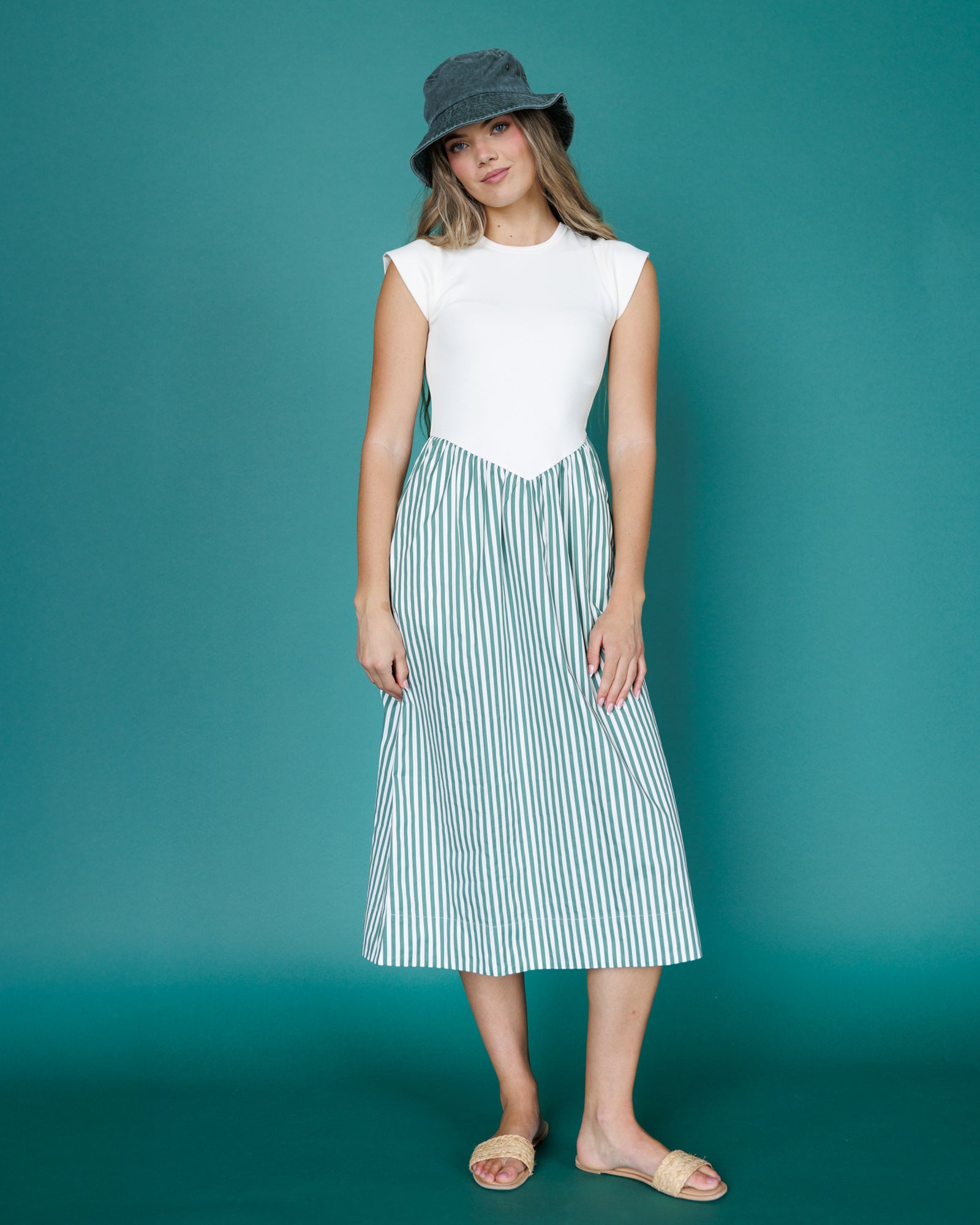 Woman wearing a white top and green striped skirt against a teal background