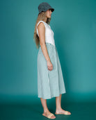 Woman wearing a white sleeveless top and green and white striped skirt against a teal background