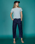 Person wearing a light gray t-shirt and dark blue jeans against a teal background