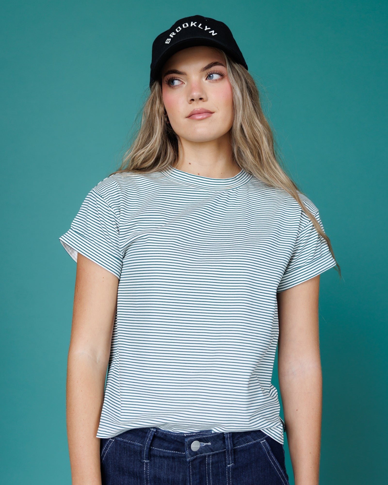 Woman wearing a striped t-shirt and a cap with 'Brooklyn' text on a teal background