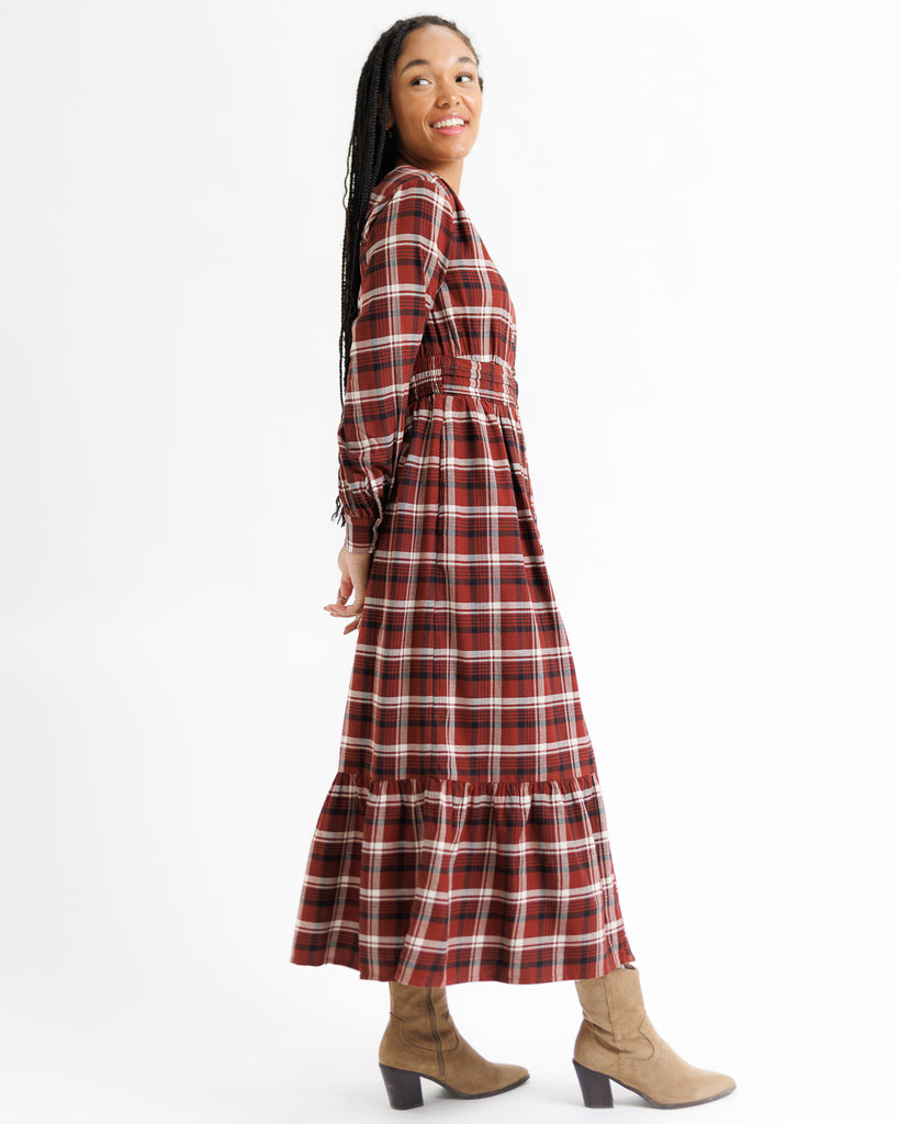 Woman wearing a red and white plaid dress with brown boots on a white background