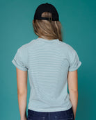 Person wearing a striped t-shirt and black cap on a teal background