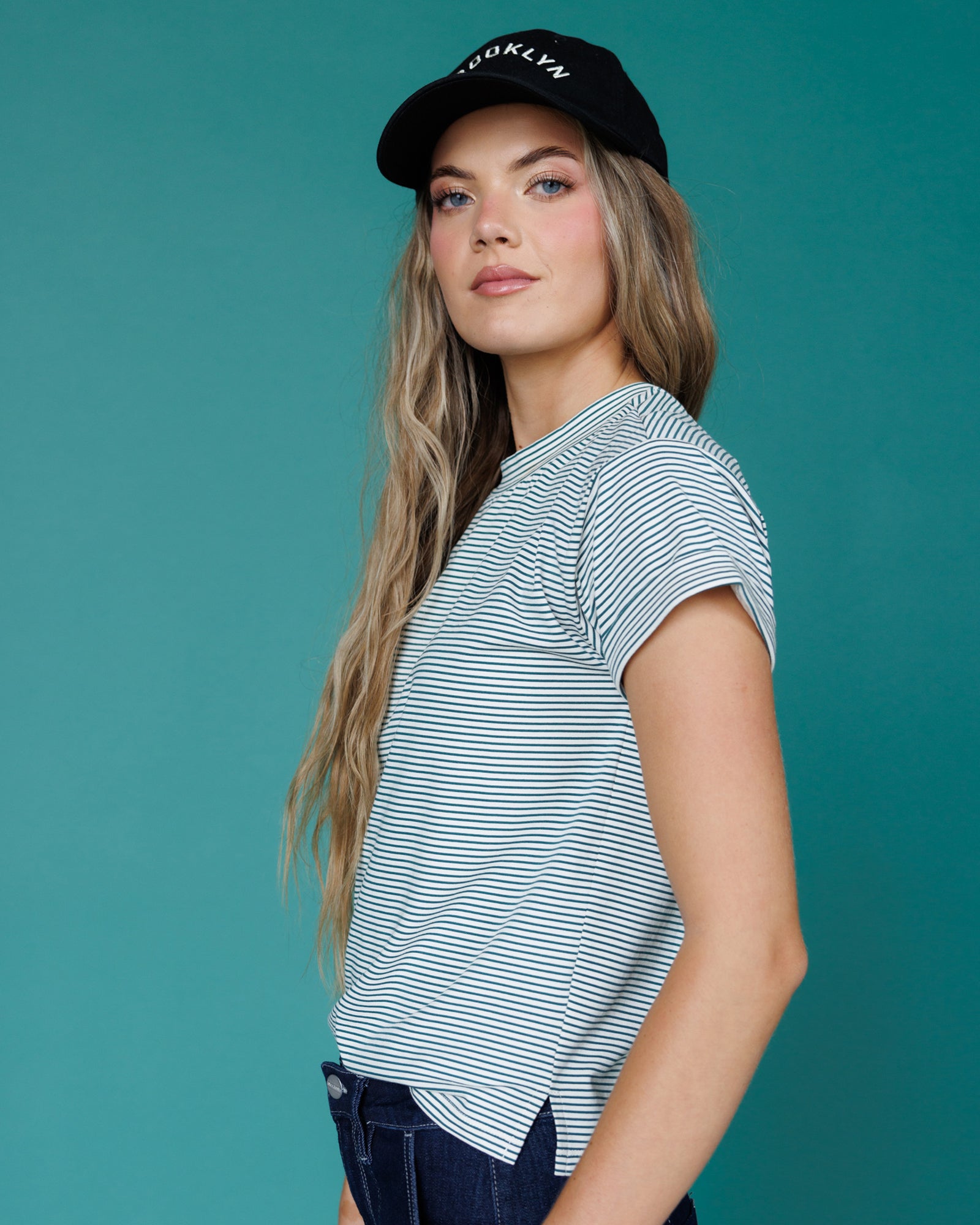 Woman wearing a striped shirt and cap against a teal background
