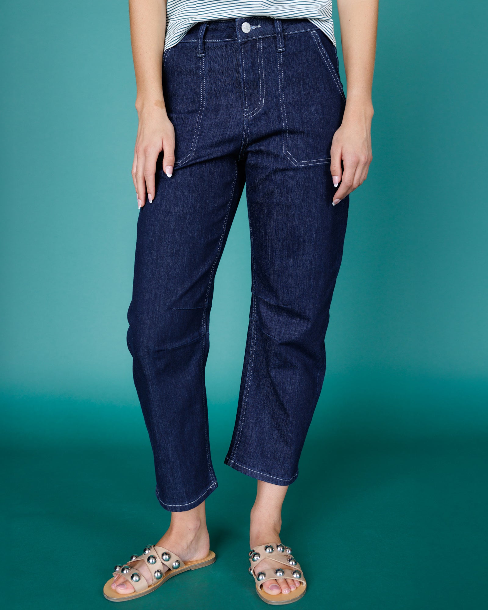 Person wearing dark blue jeans against a teal background