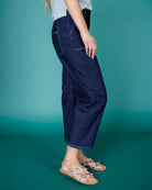 Person wearing dark blue jeans against a teal background
