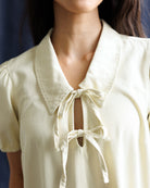 Close-up of a person wearing a light-colored blouse with a bow detail.