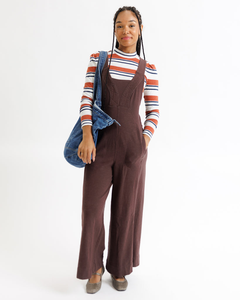 Woman wearing brown overalls with a striped sweater and denim jacket on a white background