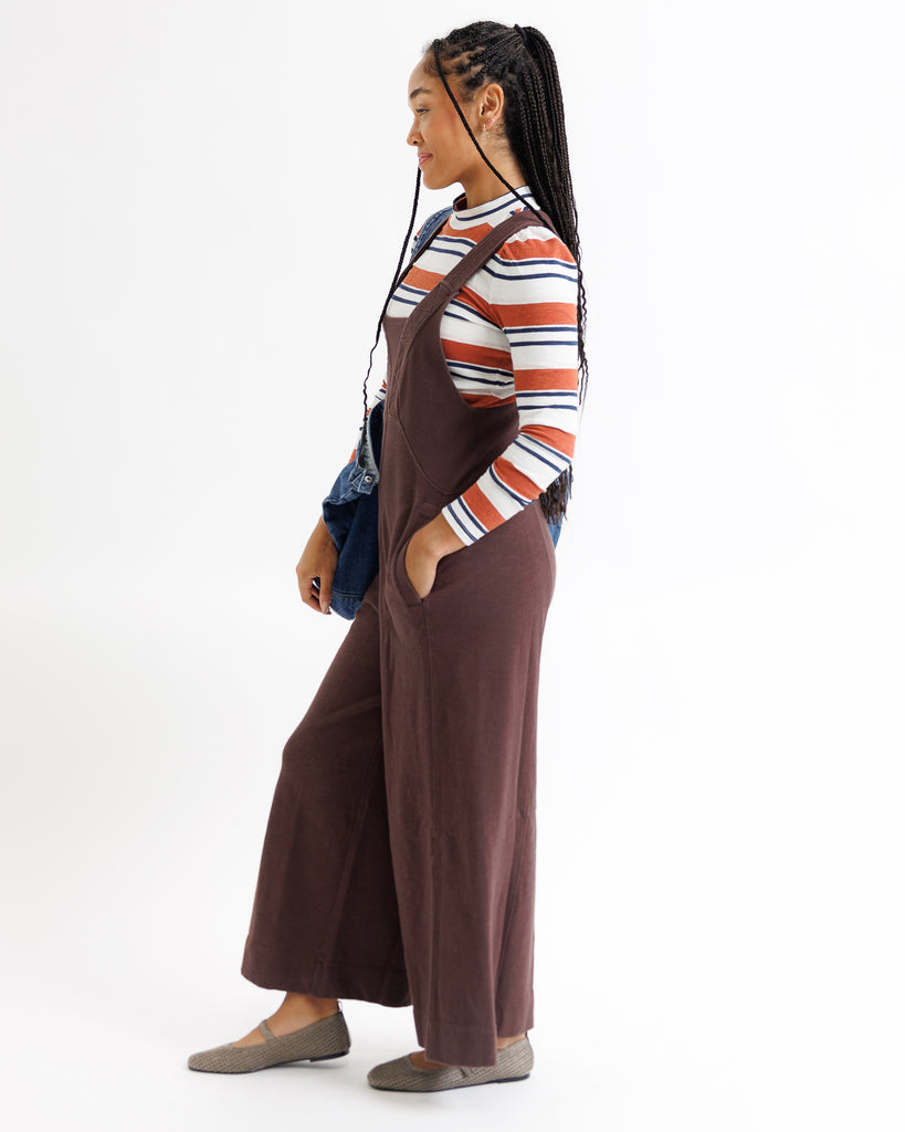 Person wearing a brown overalls and striped shirt on a white background