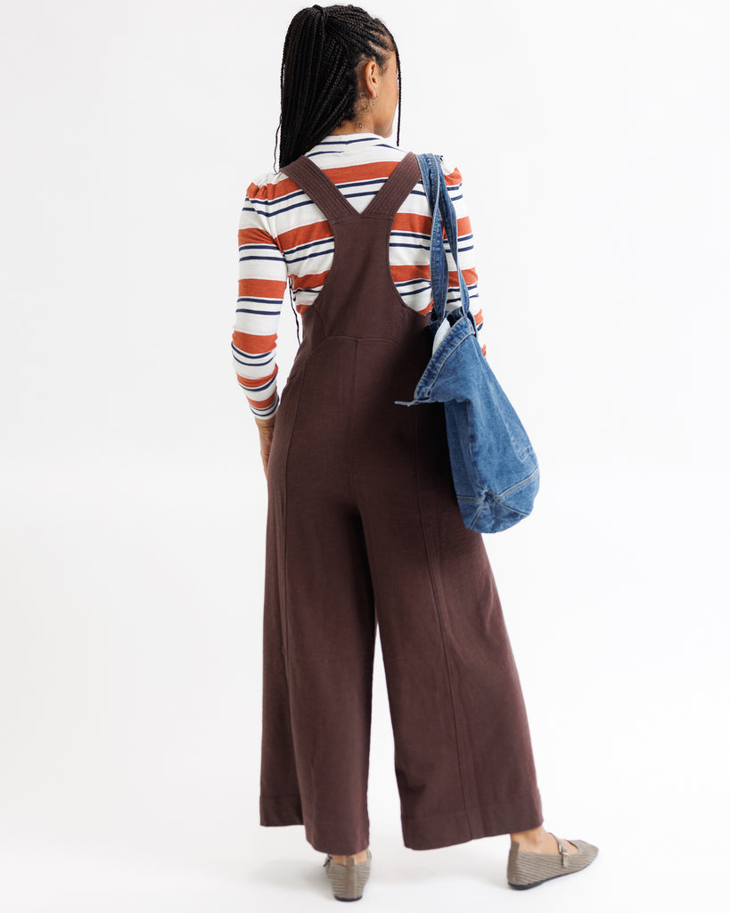 Person wearing a brown jumpsuit with a striped shirt and carrying a blue bag on a white background