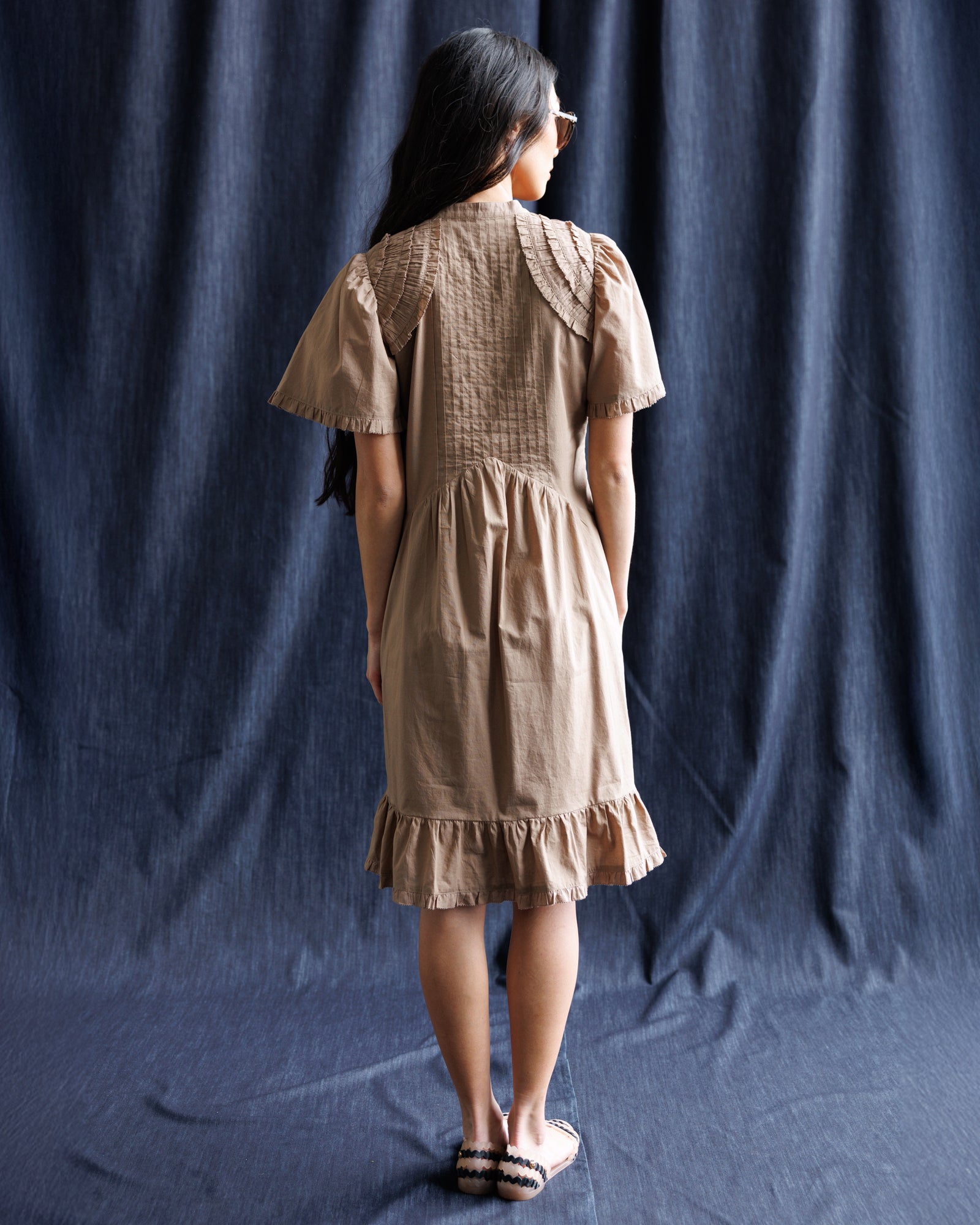 Woman wearing a beige dress standing against a dark blue curtain