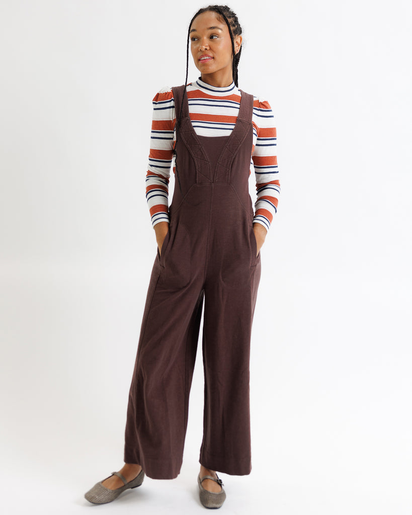 Person wearing brown overalls and a striped sweater on a white background
