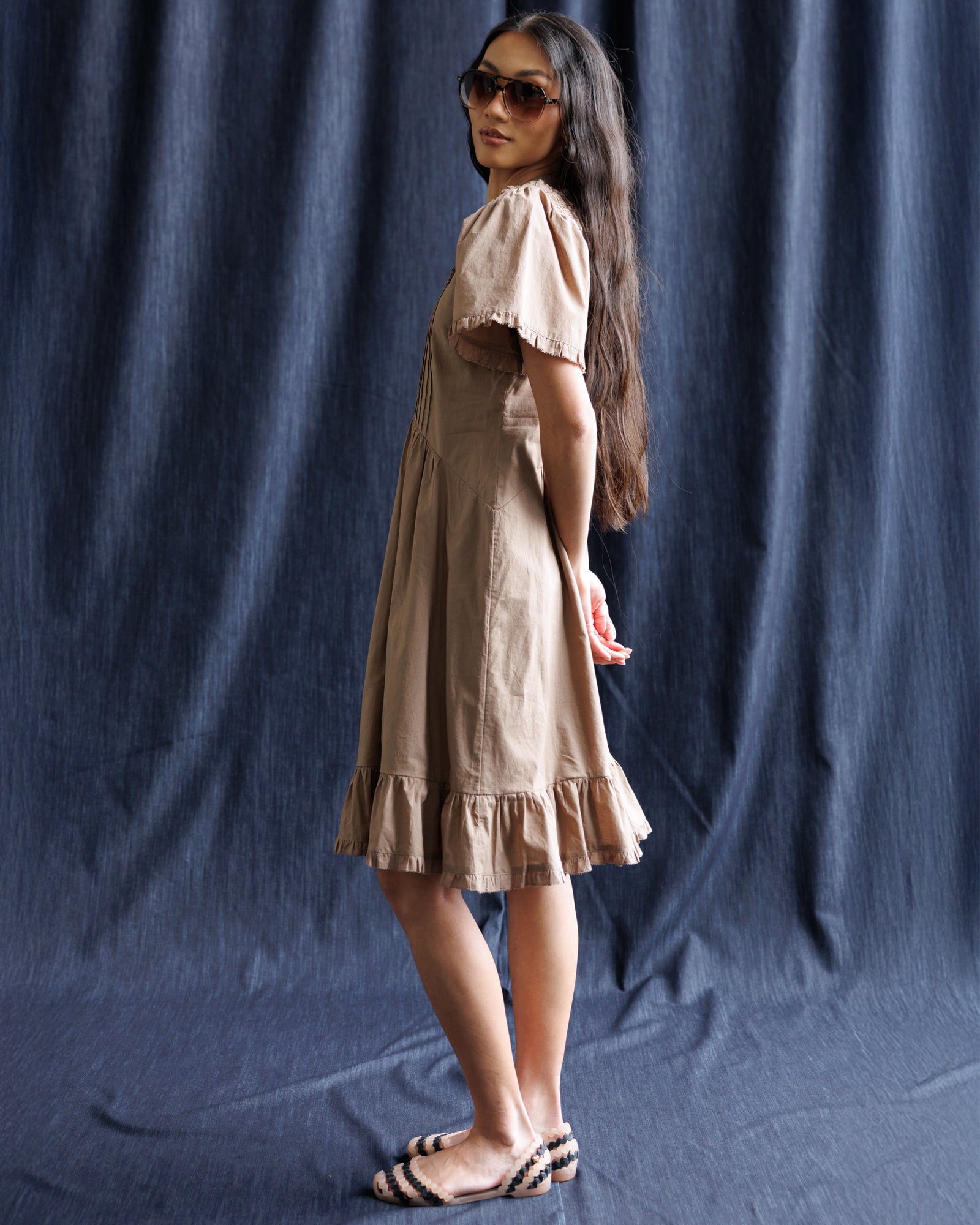 Woman wearing a beige dress against a dark blue curtain