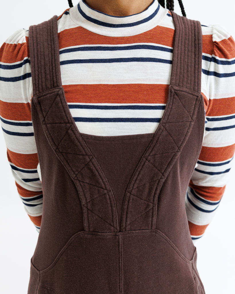 Person wearing a striped shirt with a brown knitted overall dress.