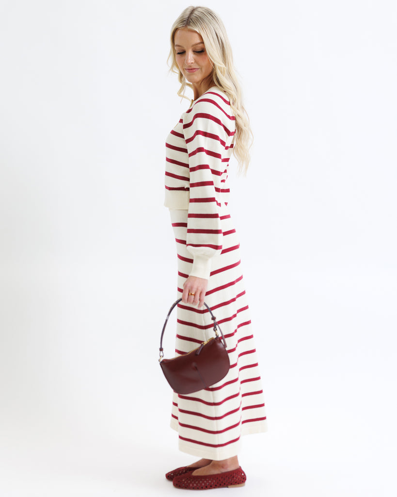 Woman wearing a red and white striped dress holding a brown handbag on a white background
