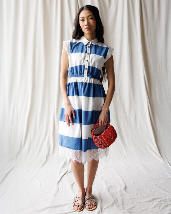 Woman wearing a blue and white striped dress holding a red bag against a white background