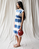 Woman wearing a blue and white striped dress holding a red handbag against a plain background