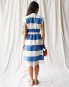 Woman wearing a blue and white striped dress against a white curtain background