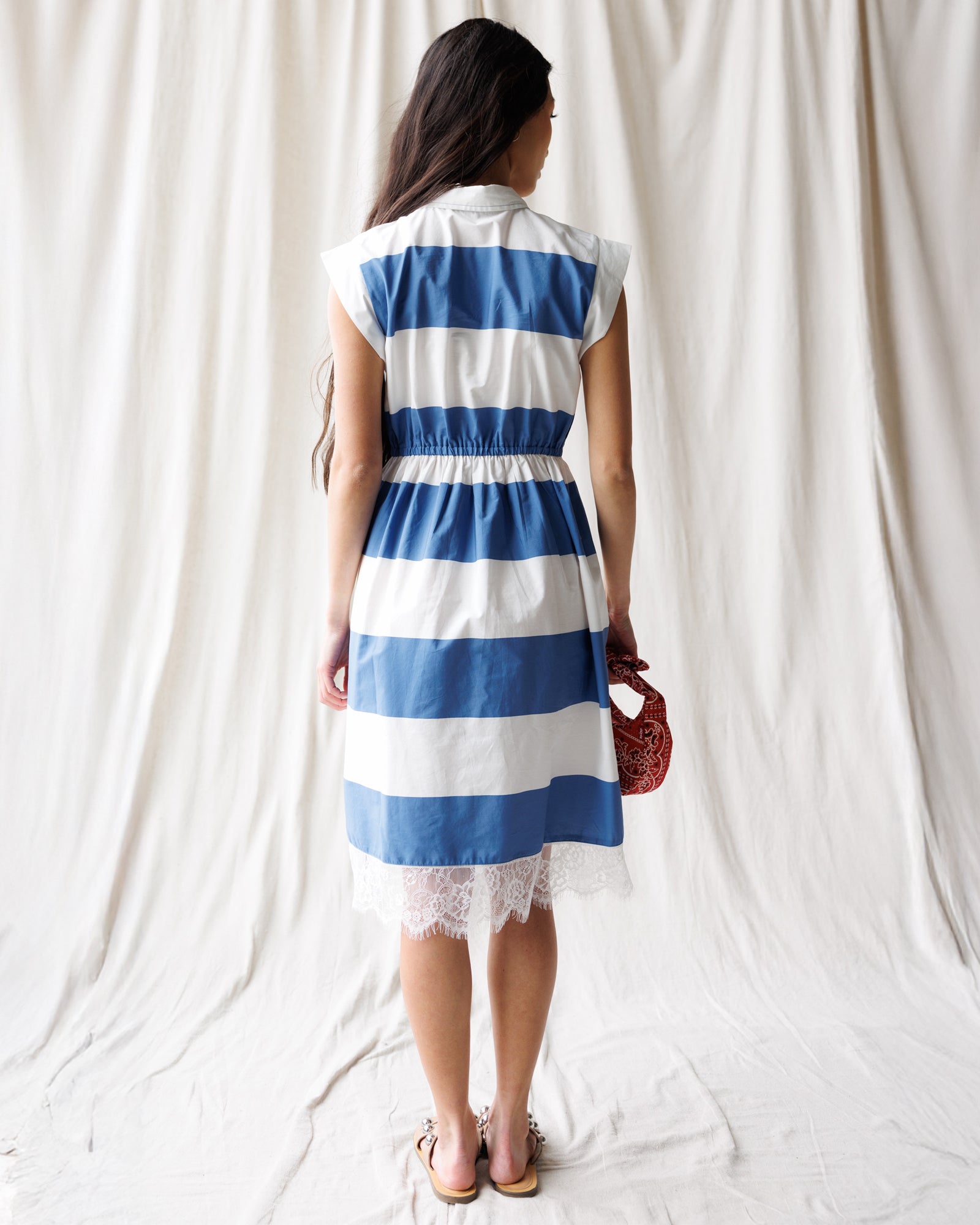 Woman wearing a blue and white striped dress against a white curtain background