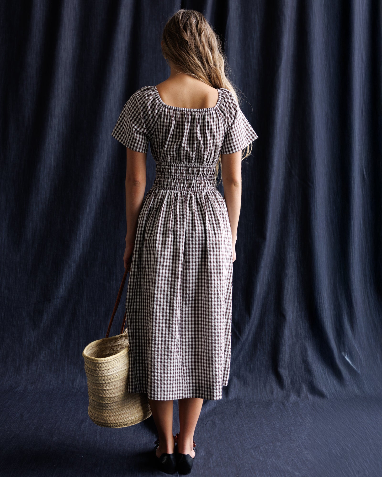 Woman in a checkered dress holding a basket against a dark background