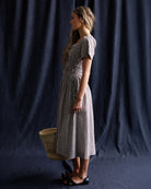 Woman wearing a checkered dress holding a woven basket against a dark background