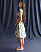 Woman wearing a floral dress standing against a dark blue curtain