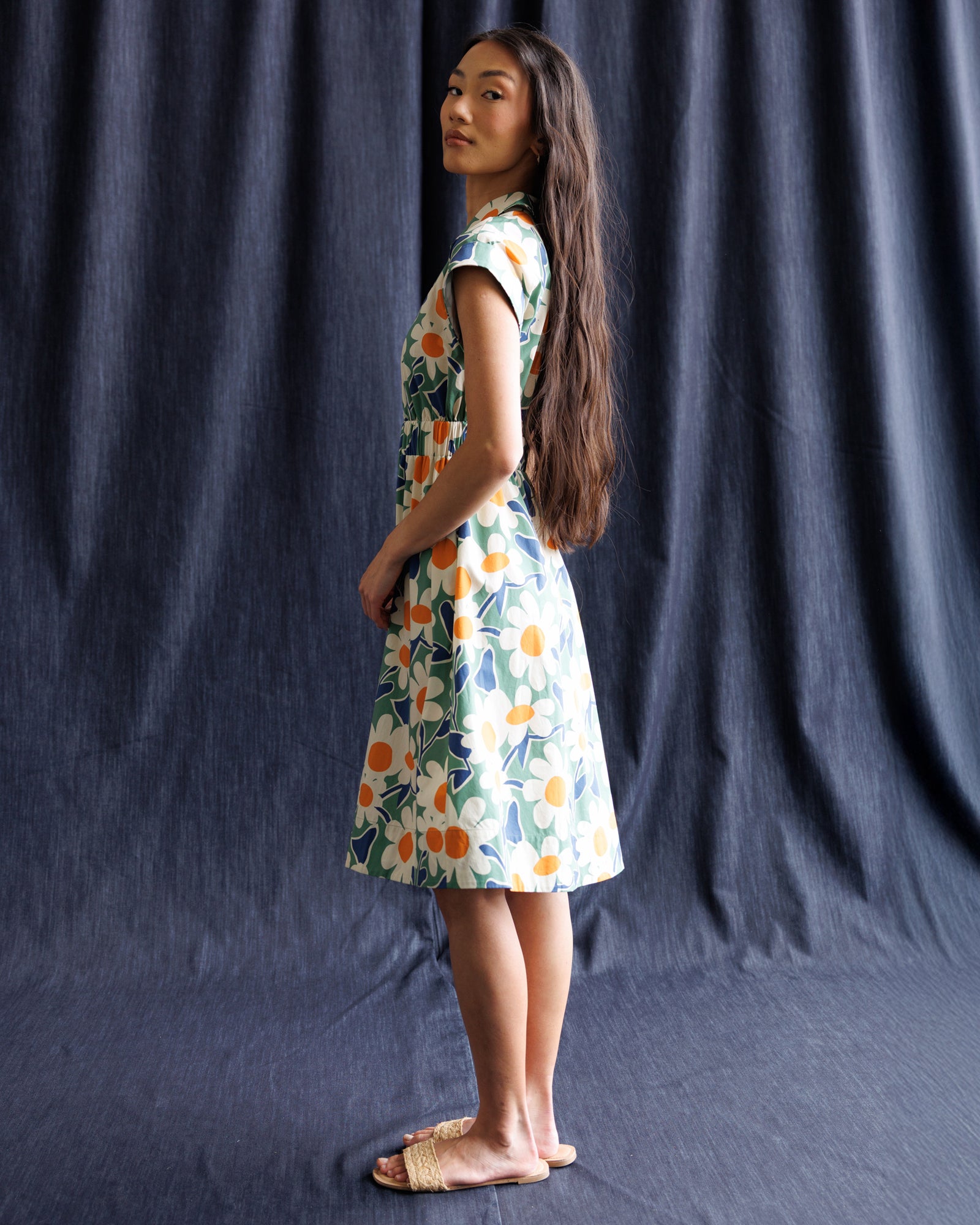 Woman wearing a floral dress standing against a dark blue curtain
