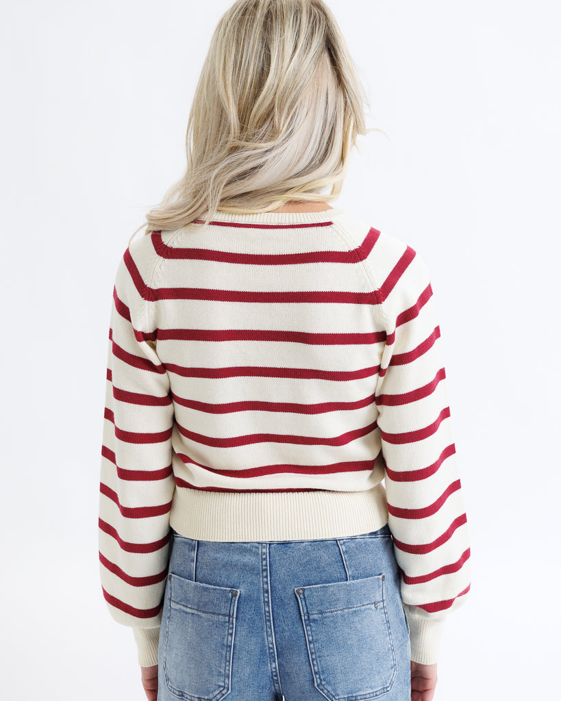 Person wearing a red and white striped sweater with blue jeans on a plain background