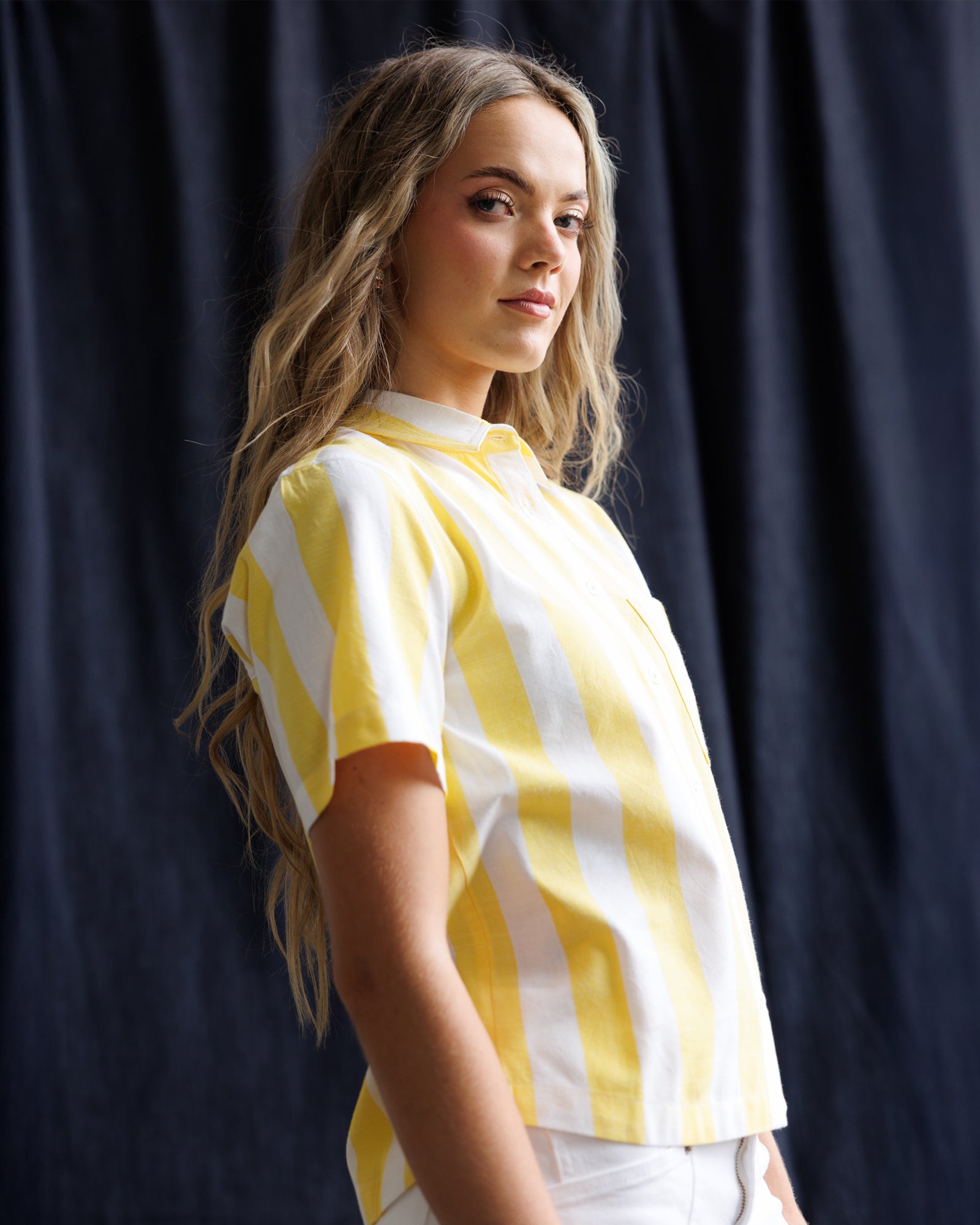 Woman wearing a yellow and white striped shirt against a dark background
