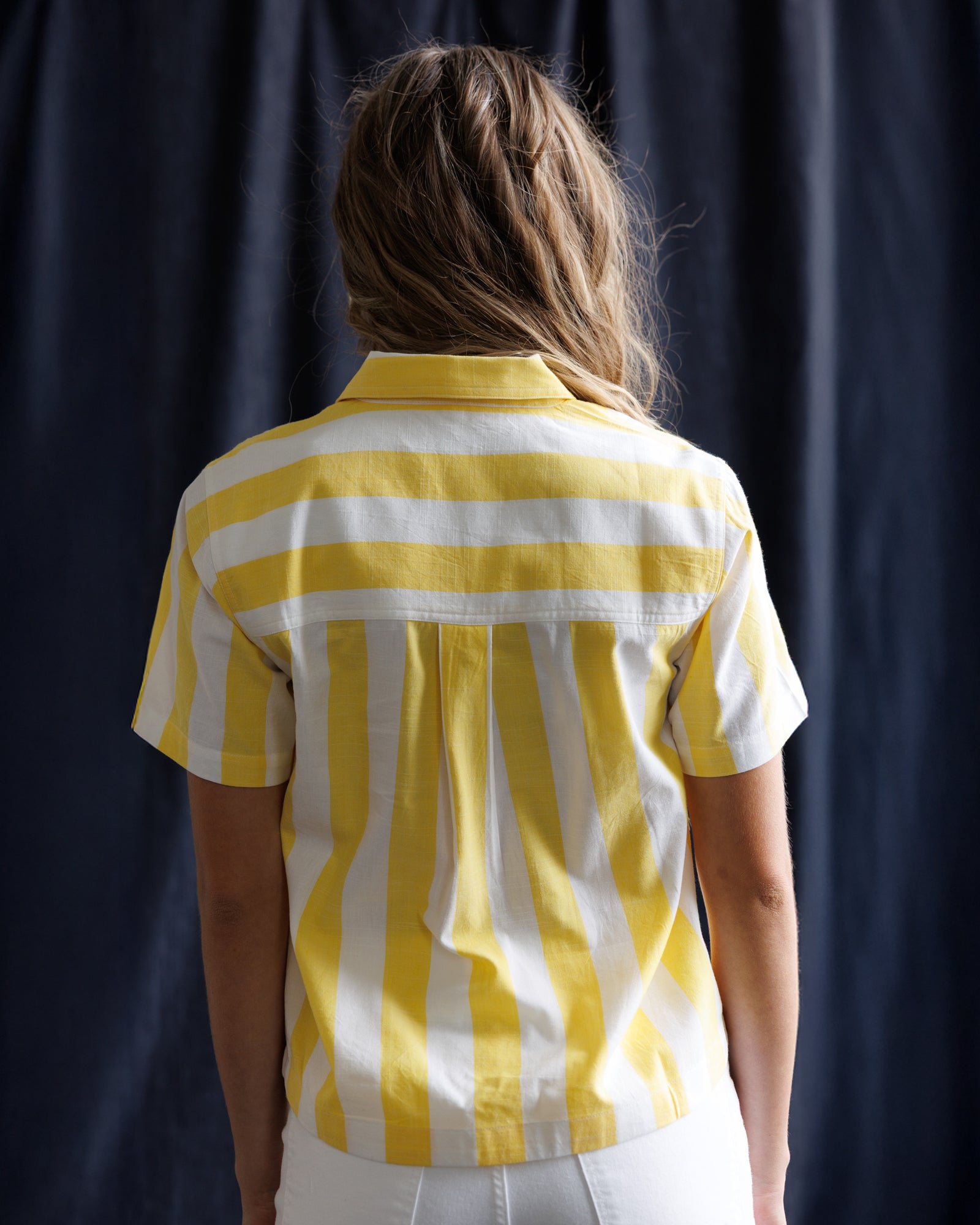 Person wearing a yellow and white striped shirt against a dark background