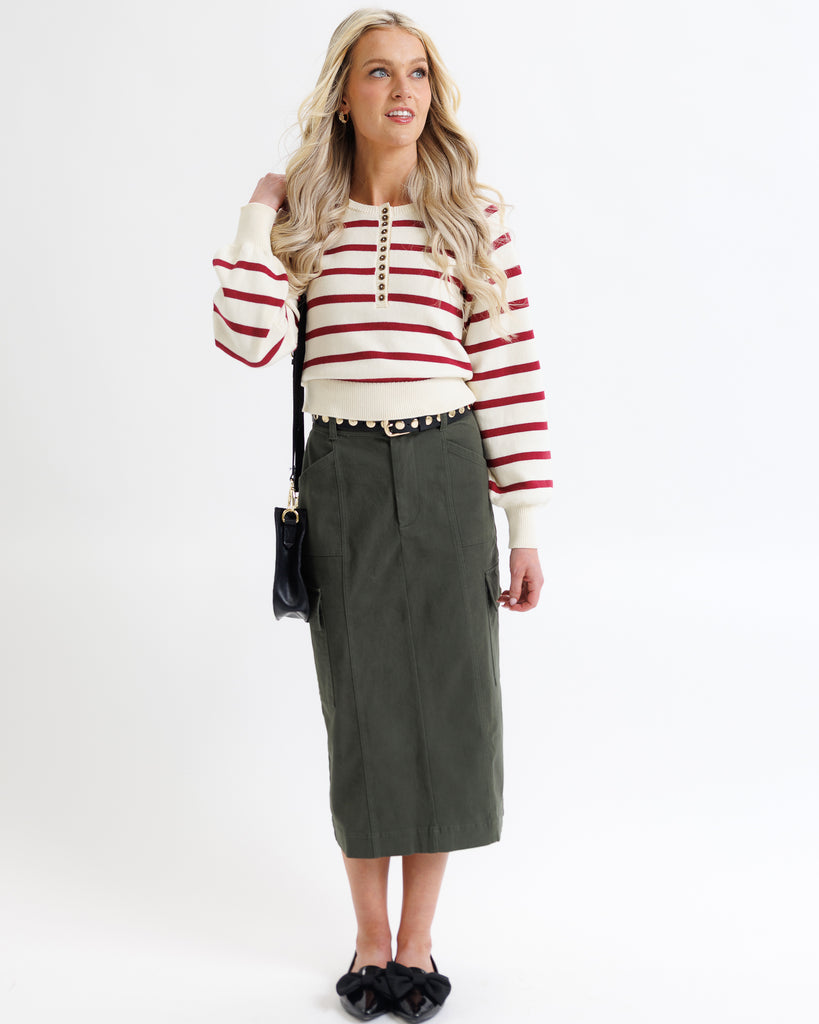 Woman wearing a red and white striped sweater with a green skirt on a white background