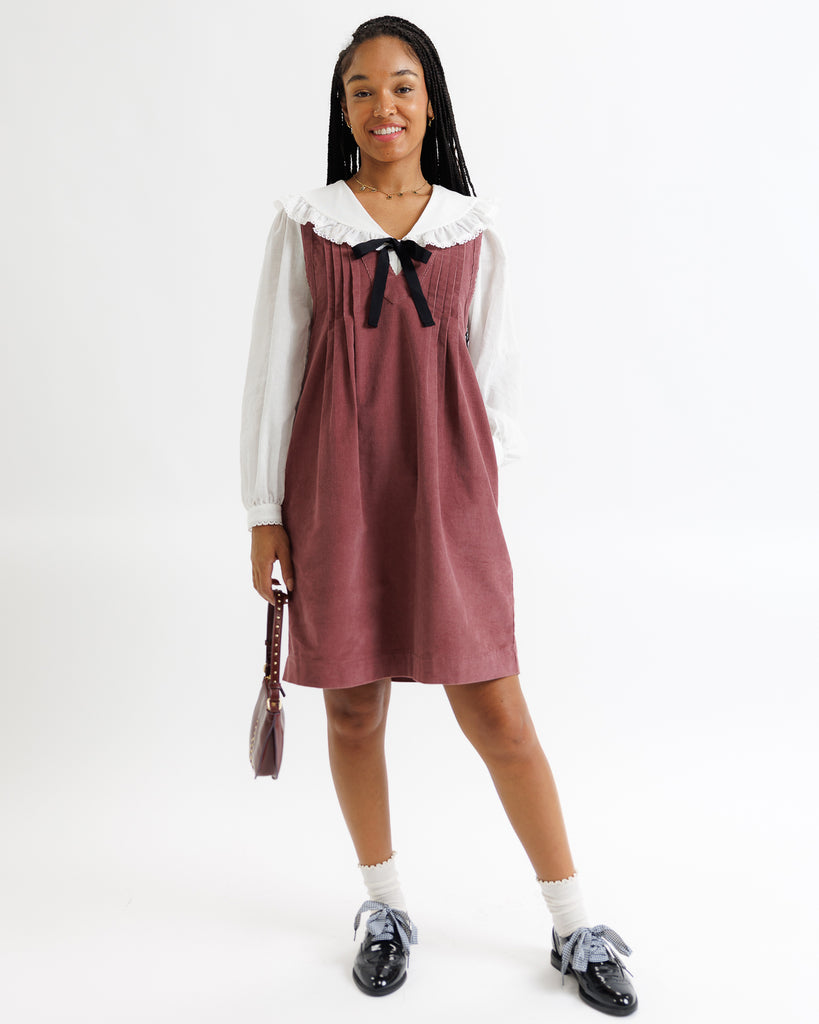 Woman wearing a maroon dress with a white blouse and black shoes on a white background