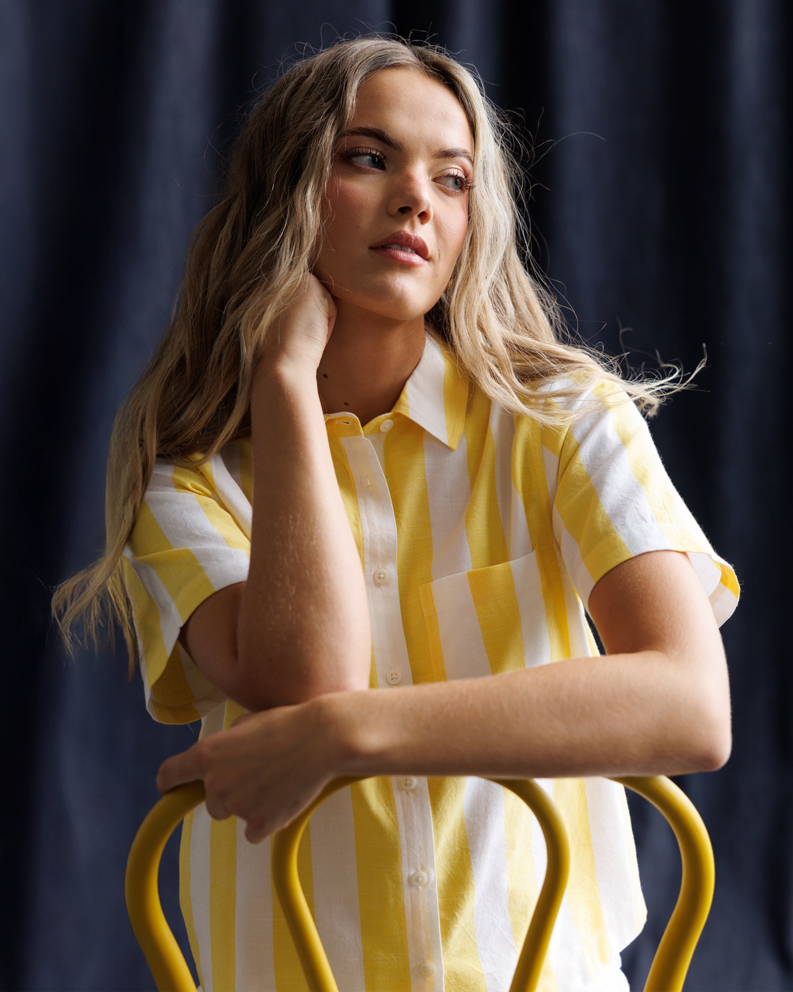 Woman wearing a yellow and white striped shirt sitting on a chair against a dark background