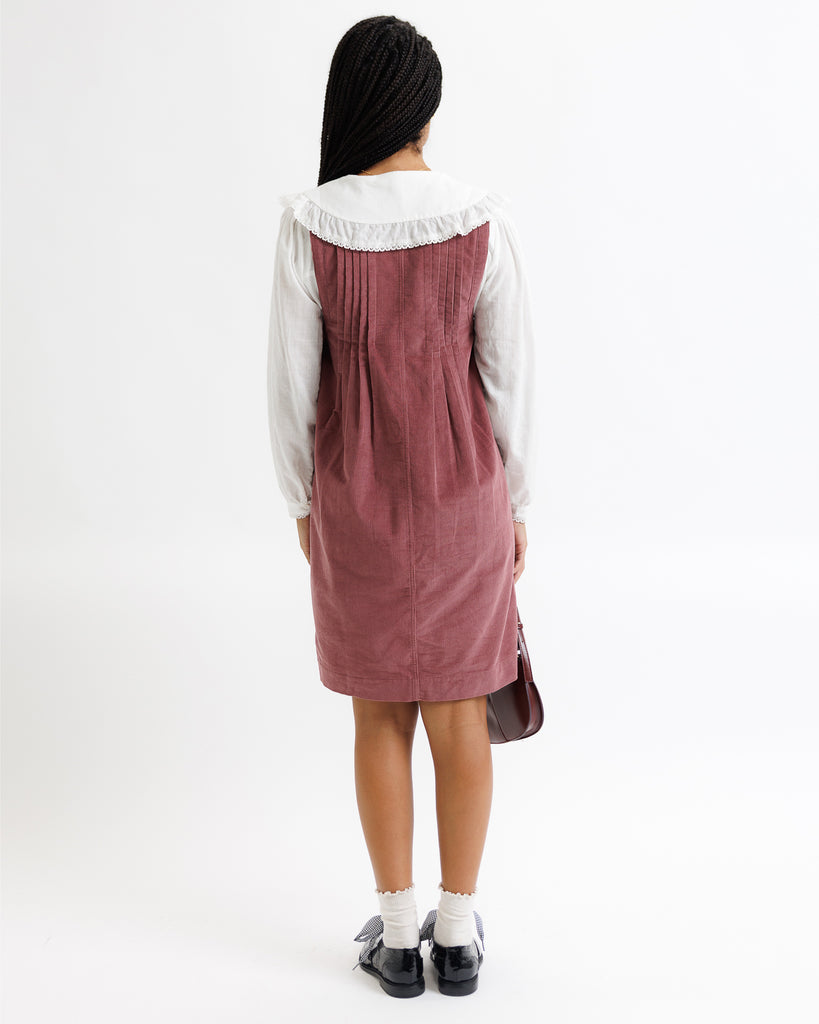 Person wearing a white shirt and maroon dress with a black headscarf on a white background