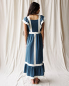 Woman wearing a blue dress with white accents against a white curtain background