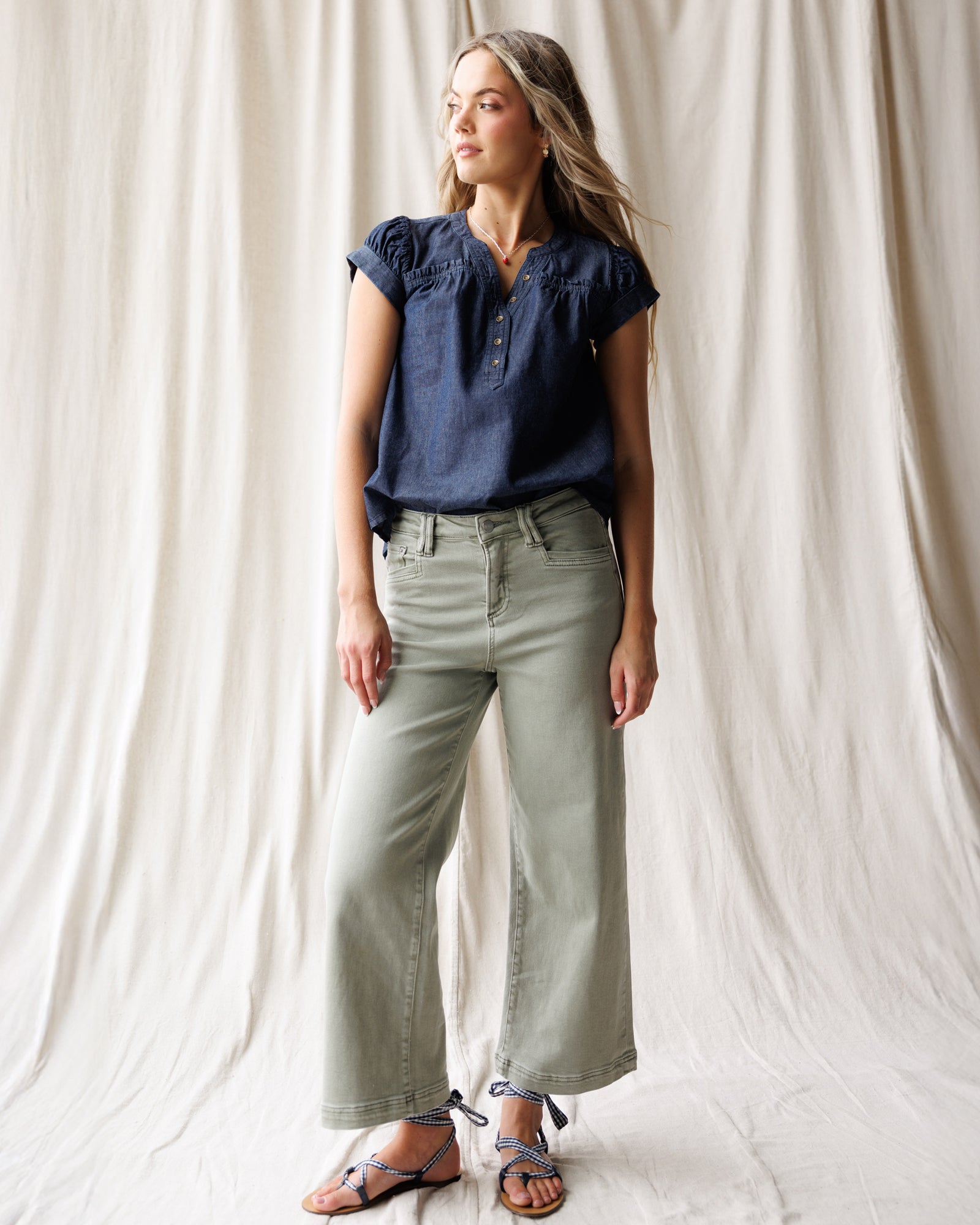 Woman wearing a navy blue top and light green pants against a white curtain background