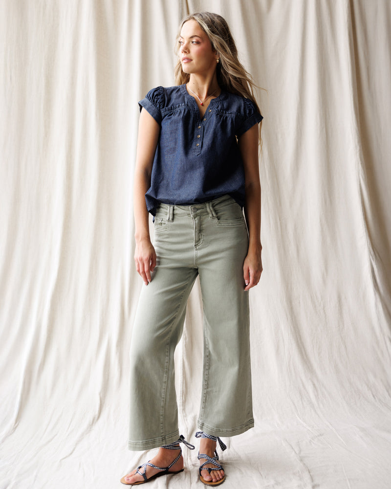 Woman wearing a navy blue top and light green pants against a white curtain background
