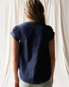 Person wearing a navy blue shirt against a white curtain background