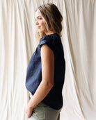 Woman wearing a navy blue sleeveless top against a white curtain background