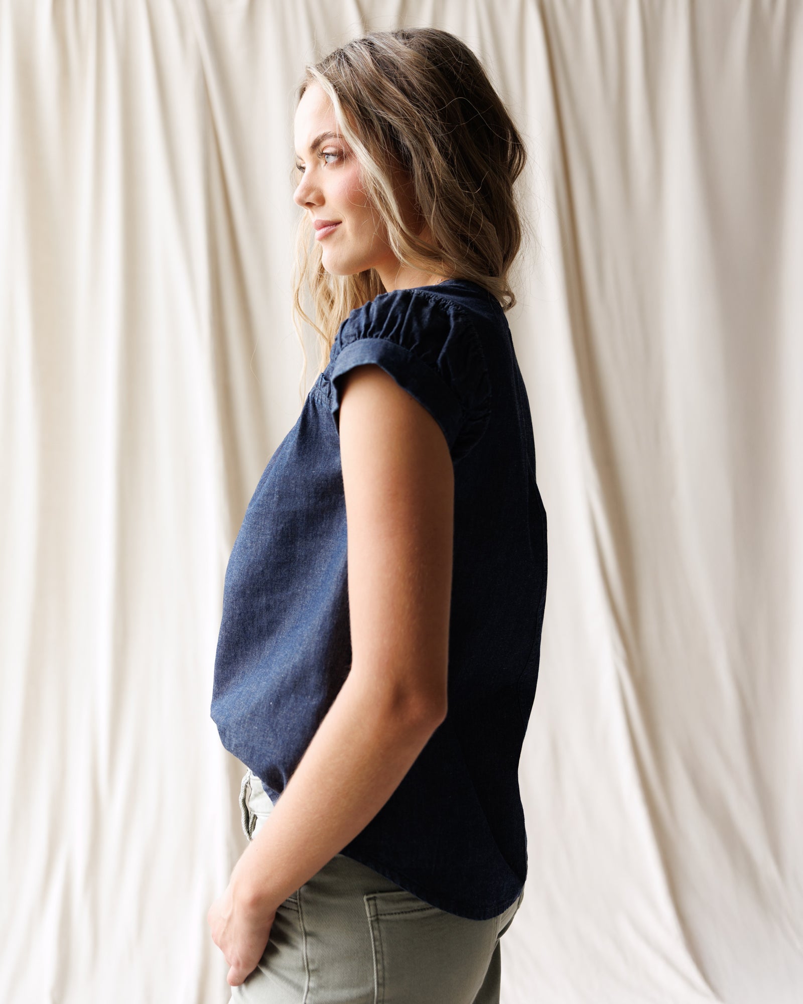 Woman wearing a navy blue sleeveless top against a white curtain background