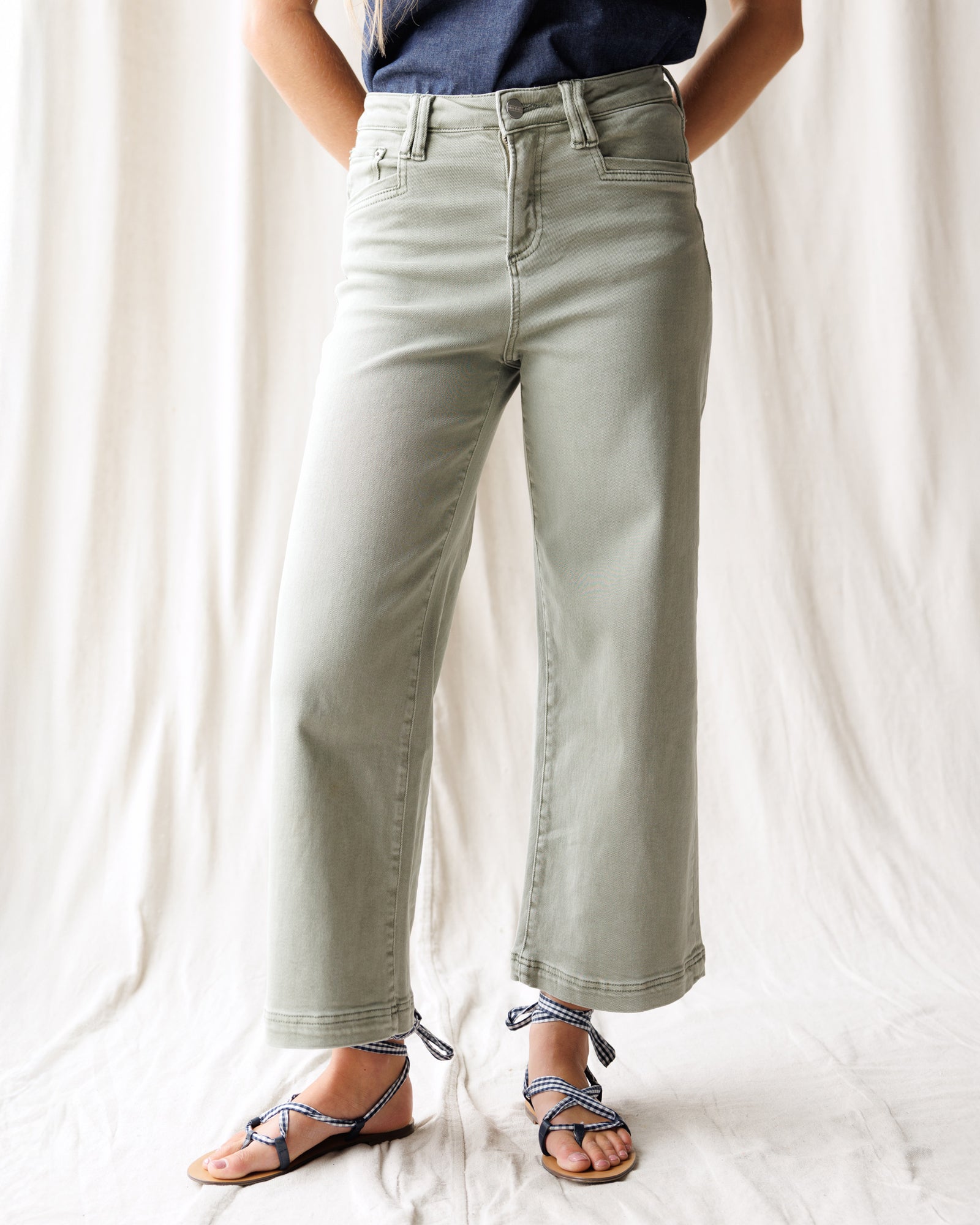 Person wearing light green jeans and a blue top against a white background