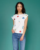 Woman wearing a white top with colorful floral patterns and blue jeans against a teal background