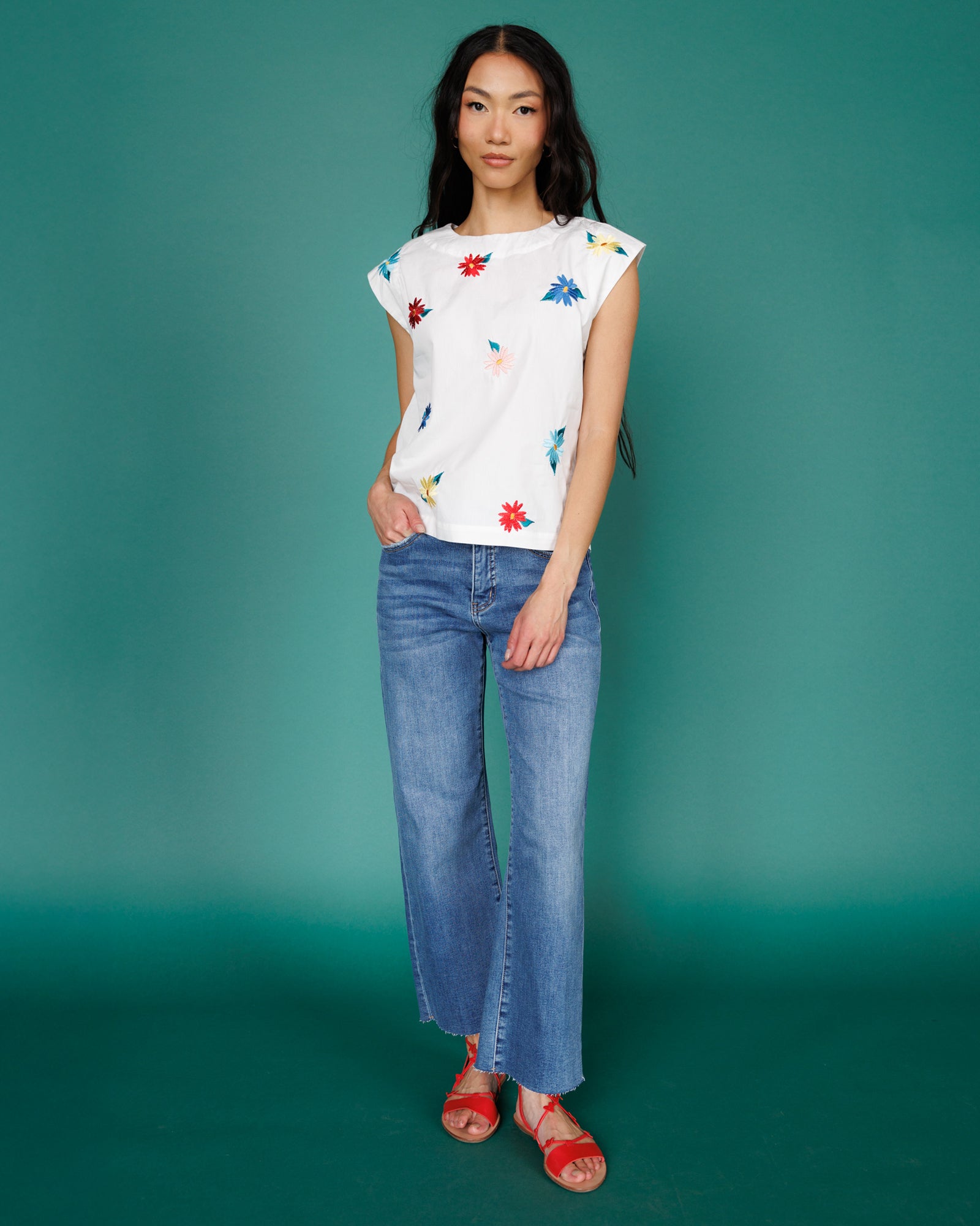Woman wearing a floral top and blue jeans against a teal background