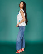 Woman wearing a white sleeveless top and blue jeans against a teal background