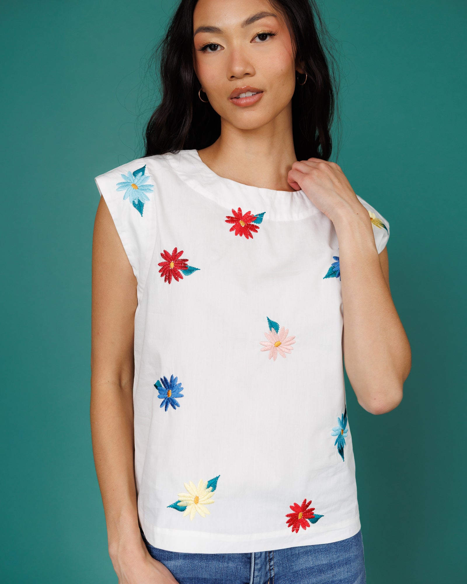 Woman wearing a white sleeveless top with colorful floral patterns against a teal background