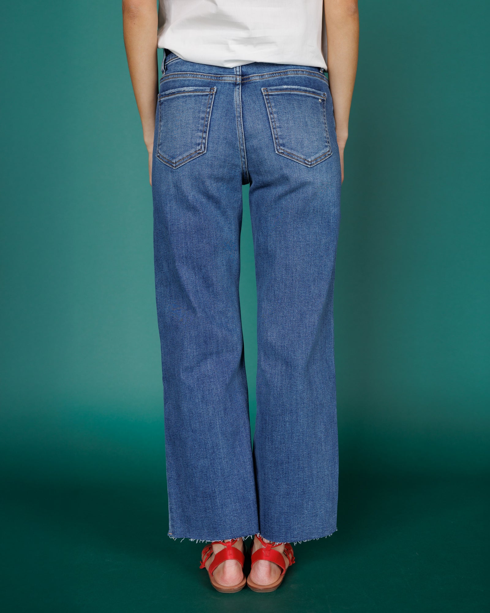 Person wearing blue jeans and red sandals on a teal background