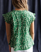 Green floral blouse worn by a person against a dark background
