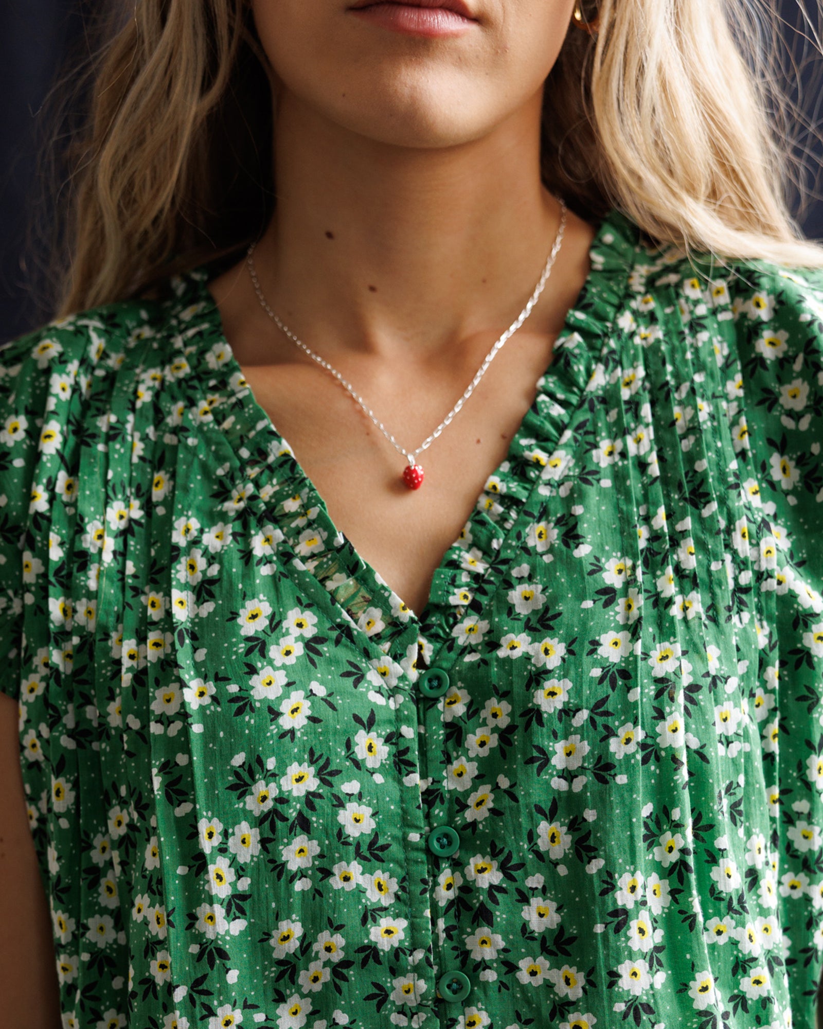 Person wearing a green floral dress with a necklace featuring a red pendant.