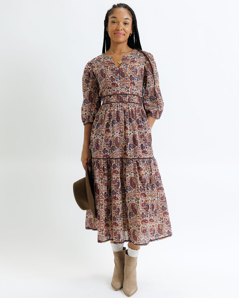 Woman wearing a patterned dress holding a hat on a white background